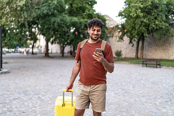 istock Young man traveling holding phone pulling luggage 2250300817
