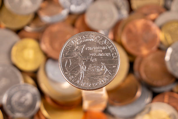 A quarter is centered among mixed coins on a table. The coins include different denominations and colors, creating a diverse collection.
