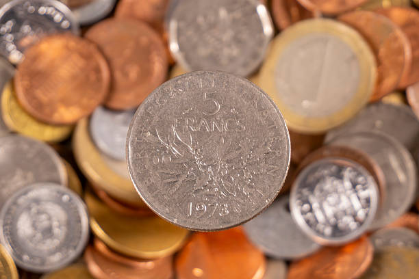 A close-up view shows a 5 franc coin among various coins from different countries and years. The coins are arranged in a scattered manner on a flat surface.