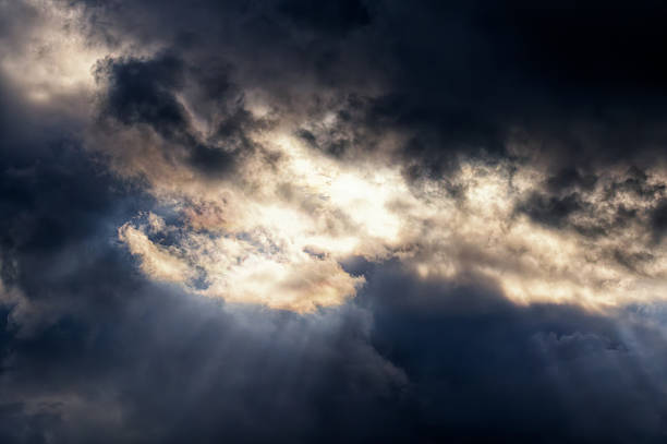 istock Dramatic dark storm clouds part as radiant sun rays pierce through the heavy sky. A powerful atmospheric scene capturing the raw energy of nature 2250315055