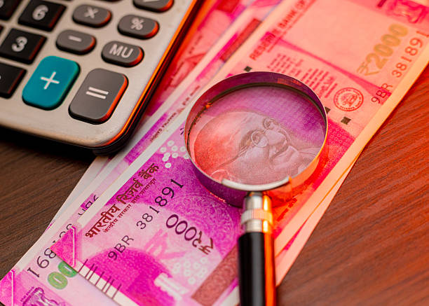 istock Image showing a  magnifying glass highlighting Mahatma Gandhi on Indian 2000 Rupee notes beside a calculator, symbolizing financial scrutiny, auditing, banking, and detailed economic analysis 2250317926