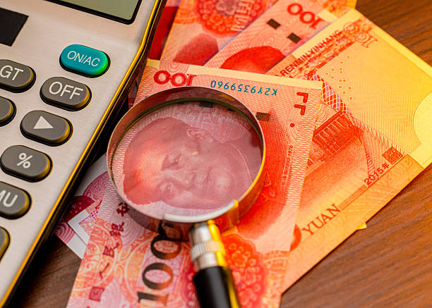 This image shows several Chinese 100-yuan banknotes featuring Mao Zedong, partially viewed through a magnifying glass. A calculator sits to the left, suggesting themes of finance and accounting