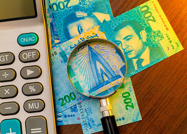 istock Image of a magnifying glass on blue Moroccan Dirham banknotes (featuring King Mohammed VI) next to a calculator, depicting financial scrutiny or calculation of North African currency. 2250318358