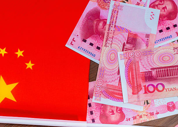 istock This image shows several pink Chinese 100 Yuan banknotes featuring Mao Zedong, scattered next to the bright red national flag of China with its yellow stars, representing Chinese currency and state 2250320696