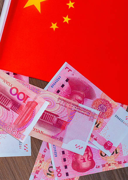 istock This image shows several pink Chinese 100 Yuan banknotes featuring Mao Zedong, scattered next to the bright red national flag of China with its yellow stars, representing Chinese currency and state 2250320697