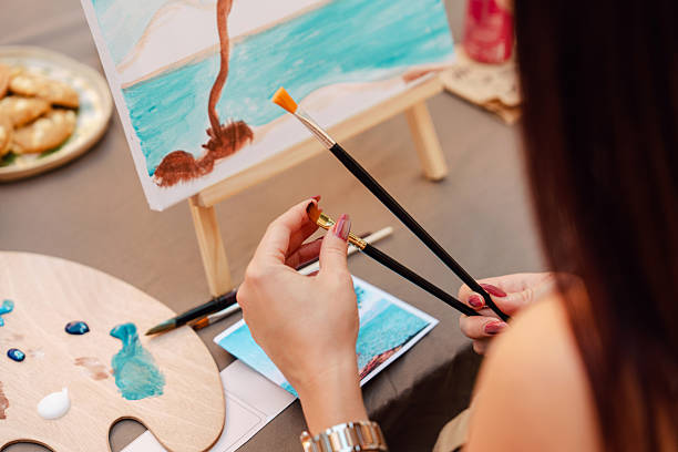 istock Woman's hands holding paintbrushes while painting outdoors in art class 2250321821