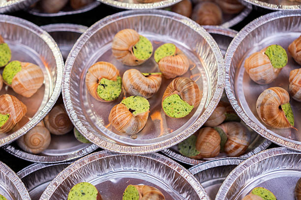 Close-up of traditional escargot in aluminum trays, prepared with garlic and herb butter, ready for baking or serving.