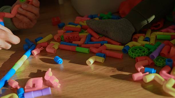 Child Hands Playing with a Pile of Colorful Plastic Construction Toy Blocks and Tubes on a Wooden Floor,Creating,Learning,and Developing Motor Skills through Creative Play