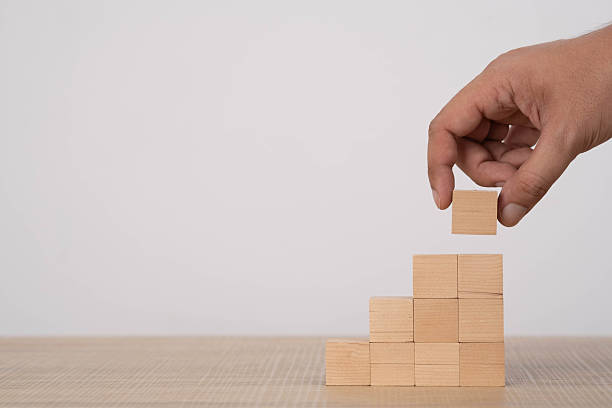 istock Hand placing a wooden block on a stepped structure symbolizes growth, progress, business development, strategic planning, and building success through step-by-step improvement and constructive effort. 2250326060