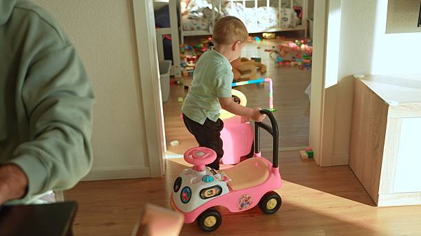 Young Toddler Staying Active,Pushing a Pink Toy Car through a Doorway into a Messy Playroom Filled with Toys,Showcasing Childhood Energy and a Busy Family Home Environment