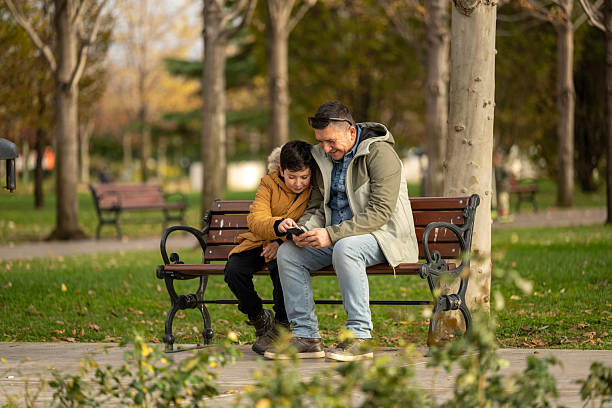 istock Father and son playing with mobile phone on bench in city park 2250344585