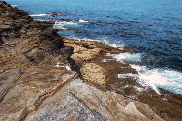 istock Dynamic high angle view of layered, eroded rock strata meeting the deep blue ocean. White waves crash against the rugged shoreline 2250350220