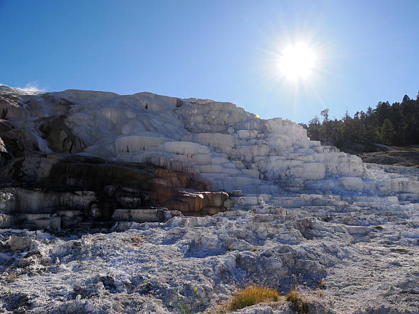 A bright sun starburst shining over the stark white travertine landscape of Mammoth Hot Springs in Yellowstone National Park.
