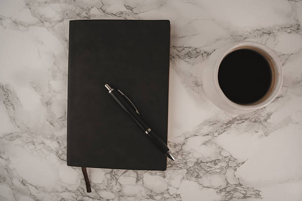 istock A black notebook and a pen rest on a smooth marble surface near a white cup filled with dark coffee, creating a focused and calm workspace in the morning 2250354878