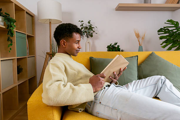 istock Young man relaxing on sofa reading book at home 2250362939