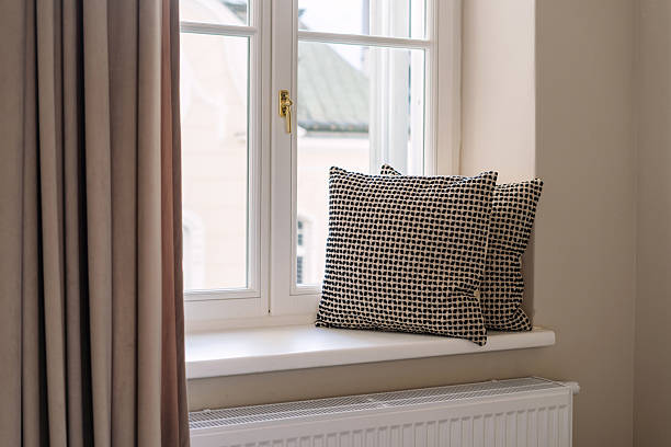 Soft decorative cushions rest on a windowsill, enhancing the cozy atmosphere of the living room or bedroom. Natural light filters in through the curtains, inviting comfort and relaxation at home space