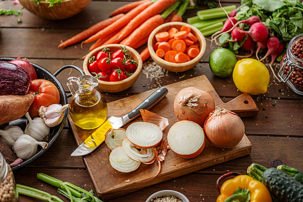 istock Vegetables, cutting board and cooking oil. High angle view of kitchen table with fresh and healthy ingredients for salad or vegan meal preparation. Whole and sliced organic onions 2250367686