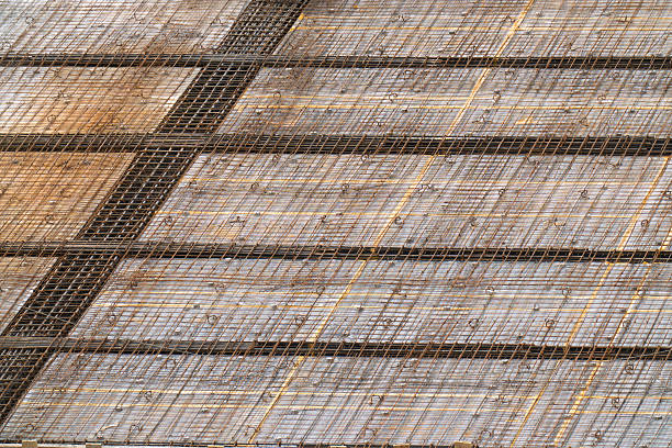 Close-up view of steel reinforcement mesh arranged in a geometric grid pattern at a construction site. The rusted rebar and structural layout highlight the industrial process of preparing concrete slabs, showcasing textures, lines, and engineering details