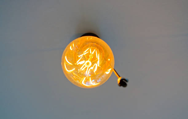 istock Glowing Vintage Edison Bulb Hanging From White Ceiling 2250393234