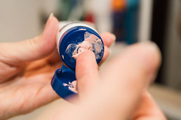 Close-up of a hand taking a small amount of dermatology cream from an open tube using a finger. Skincare and personal care concept