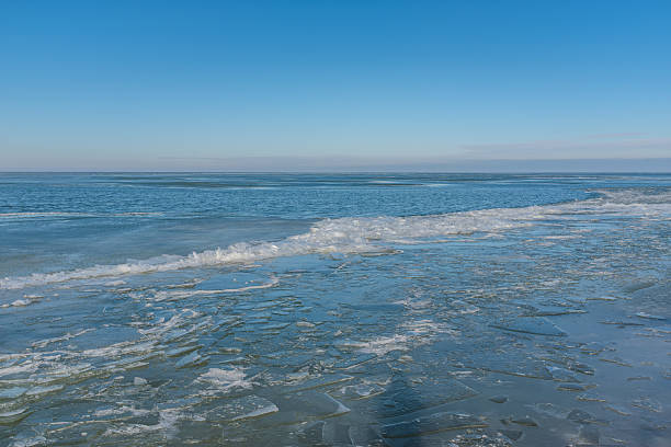 Broken plates of shore ice melt into calm blue water, where a low wave of slush marks the gentle meeting of winter and open lake.