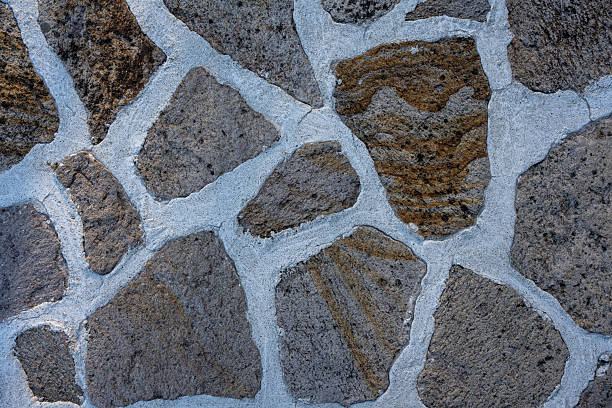 Textured background of a stone wall made from uneven, natural rocks embedded in light cement mortar.