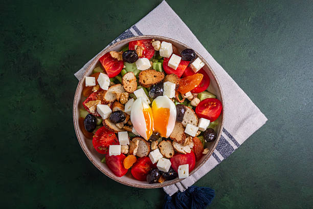 Serving of salad made with jamon slices, boiled quail eggs, soft cheese, fresh different greens and vegetables on a dish on a rustic table, top view
