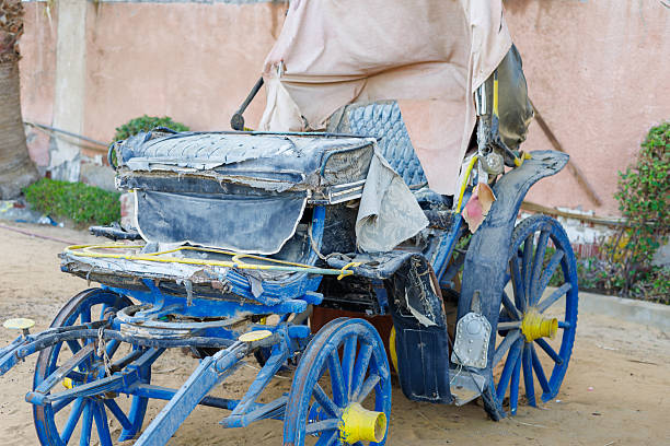 Dilapidated blue horse-drawn carriage on sandy ground.