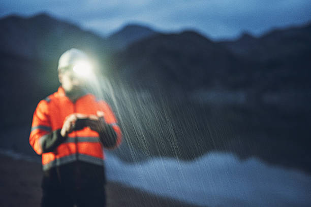 Engineer maintains hydroelectric dam in heavy rain outdoors at night using AI on waterproof device & headlamp, ensuring efficiency & sustainability of hydroelectric power plant