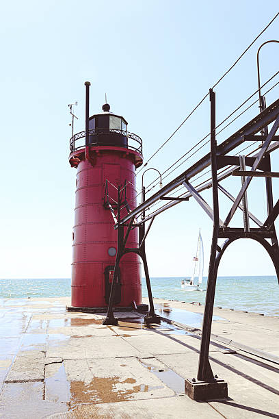 A bright red lighthouse stands on a pier along Lake Michigan in South Haven, Michigan. The historic structure contrasts beautifully with the blue sky and water, surrounded by waves