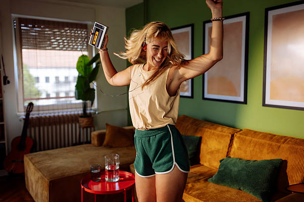 A young woman dances joyfully in a cozy living room, enjoying music from a cassette player; Casual, retro vibe with a green wall, sofa, and framed art in the background