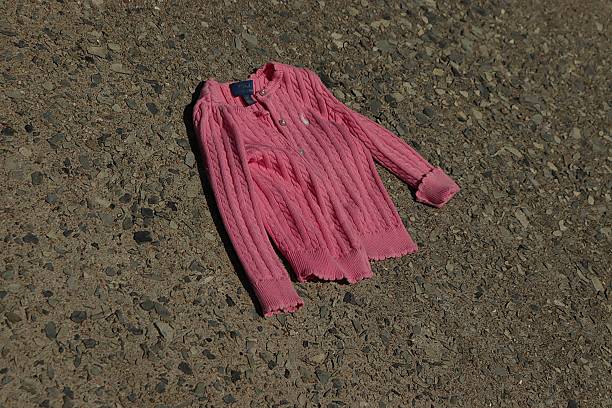 A bright pink cable-knit cardigan lies forsaken on a textured concrete surface under strong daylight, symbolizing themes of child abandonment, neglect, and forgotten belongings, creating a visual narrative filled with melancholy and emotional weight