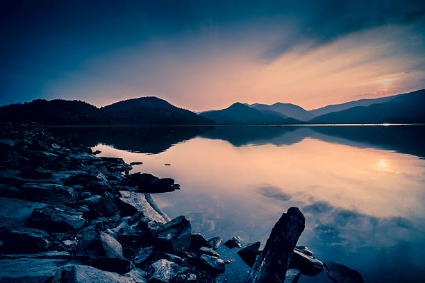 This October 2021 image shows the sunrise powering through rain clouds in Lake Tekapo, Aotearoa New Zealand. The surface of the lake is mostly calm, broken only by raindrops in the middle of the image. A bit of snow remains on Mount Edward in the distance. The reds, oranges, and yellows of this image were only visible for a few minutes because of the shifting rain clouds.