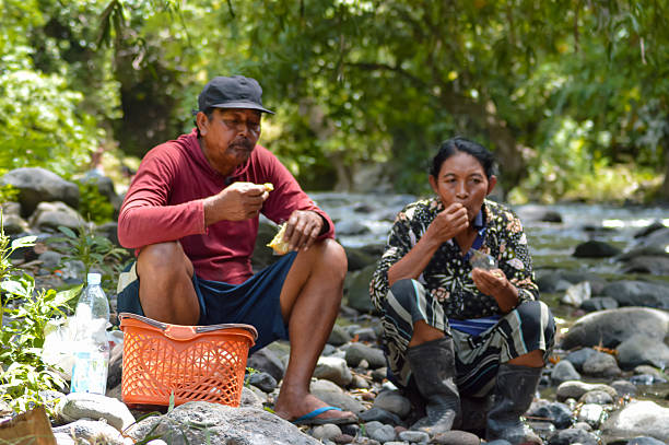istock Village Couple Resting and Snacking on Rocks beside a Shaded River 2250449712