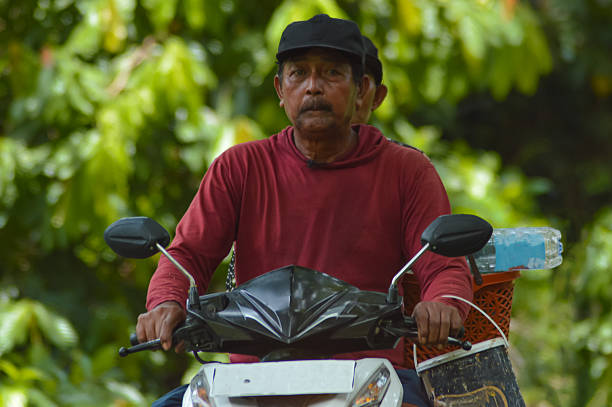 Village Man on Scooter Looking Directly at Camera in Greenery