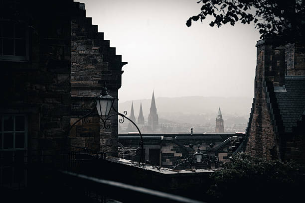 Edinburgh, Scotland - June 29, 2022: Moody, overcast view from Edinburgh Castle overlooking the city’s historic skyline. The stone architecture in the foreground frames a misty panorama with multiple church spires rising through the haze. Soft rain and diffused light create an atmospheric and cinematic feel, highlighting Edinburgh’s characteristic blend of medieval structures and dramatic weather.