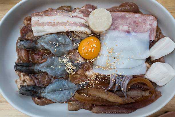 Fresh various marinated meat, seafood, and egg yolk on a white platter, prepared for Thai barbecue. Invite viewers to savor, perfect for culinary projects.