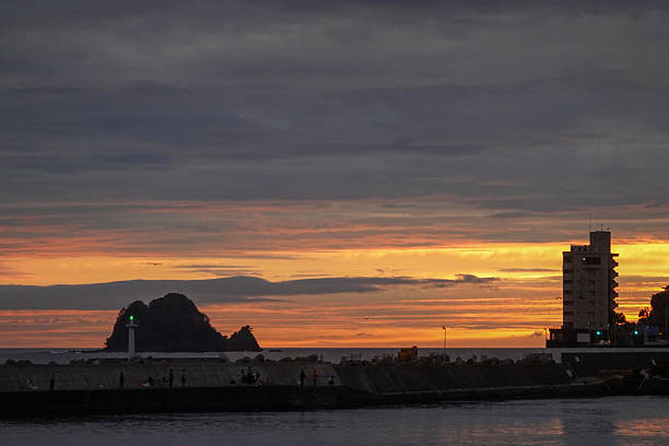 Small offshore island and long harbor wall sit beneath a deep blue hour twilight sky with fading light.