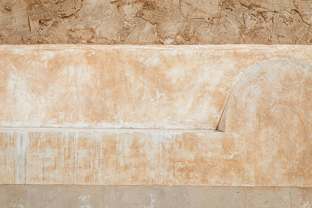 A weathered beige stucco wall with a rounded architectural curve and worn plaster texture, evoking rustic charm and a Middle East vibe. Warm neutral tones create a timeless backdrop for architecture-inspired photography.