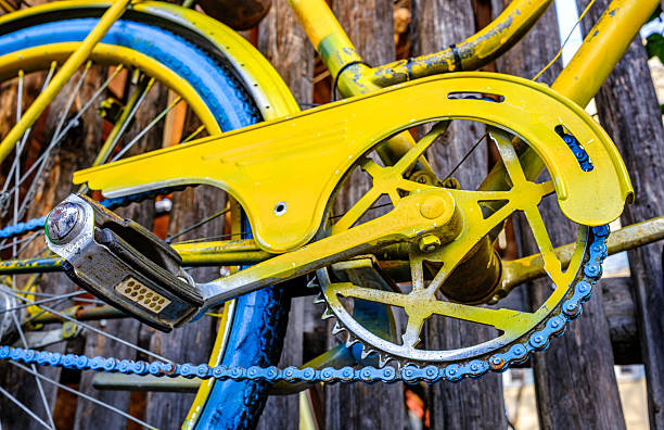 A vintage blue bicycle is propped against a colorful wall, casting shadows on the pavement. Sunlight bathes the scene, highlighting the bike's design and the warm colors of the wall.