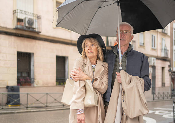 Senior couple sharing an umbrella while walking on a city street in the rain with copy space