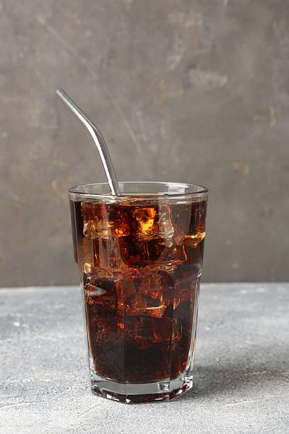 istock Refreshing cola with ice cubes and drinking straw in glass on light textured table against grey background, closeup 2250470695