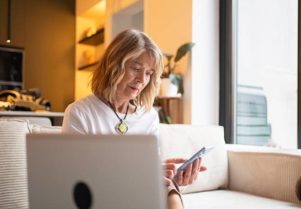 istock Senior woman using smart phone and laptop remotely 2250470772