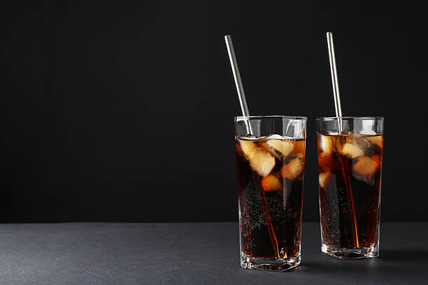 istock Refreshing cola with ice cubes and drinking straws in glasses on black table, space for text 2250470973