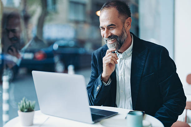 istock Smiling mature businessman using laptop in a cafeteria 2250474619