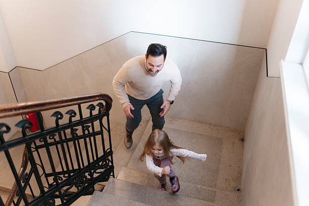 Happy father chasing his young daughter up an indoor staircase, bonding and having fun