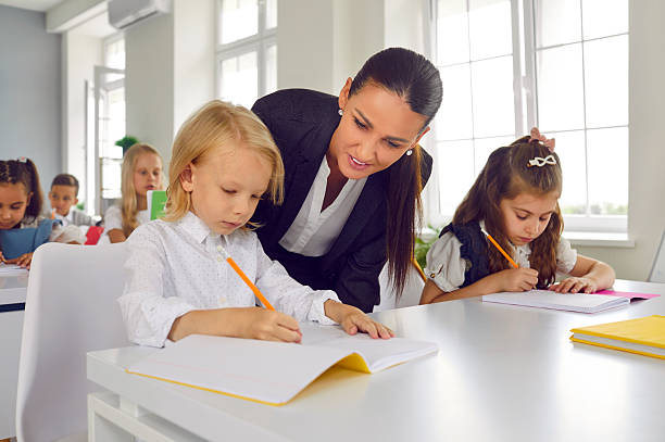 istock Friendly young female teacher helping little students with test tasks in primary school classroom. 2250480927