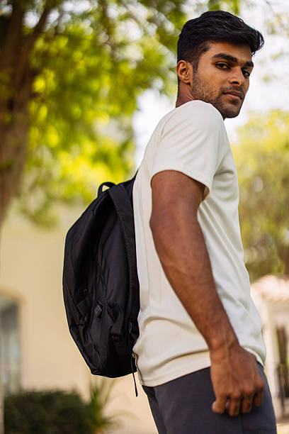 istock Young man with backpack standing outdoors in a park looking back over his shoulder 2250484421