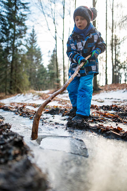 istock Little boy playing in winter forest, breaking ice on frozen puddle 2250484677