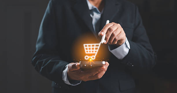 istock Businessman using smartphone with a glowing virtual shopping cart icon, representing mobile ecommerce, digital purchasing, online retail transactions and modern digital business solutions. 2250486739